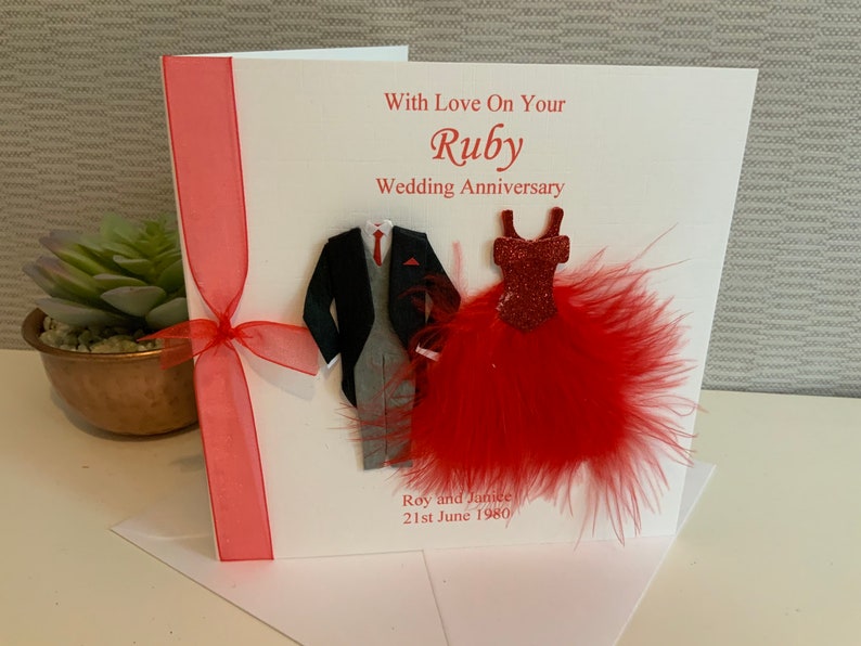 May include: A white card with a red ribbon and a red feather boa. The card says "With Love On Your Ruby Wedding Anniversary" and "Roy and Janice 21st June 1980".