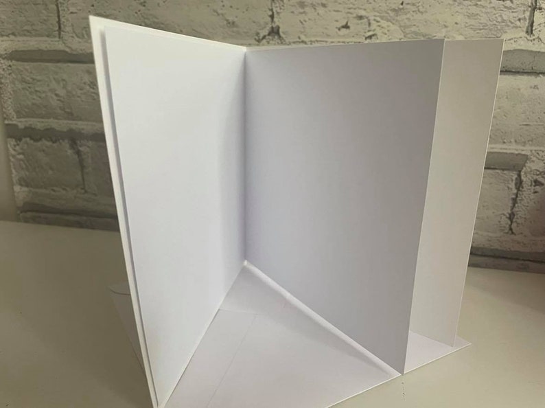 Pu&ograve; includere: Un biglietto bianco piegato a met&agrave; con interno ed esterno vuoti. Il biglietto &egrave; piegato in modo da creare una forma triangolare.