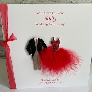 May include: A white card with red ribbon and a red feather boa. The card says "With Love On Your Ruby Wedding Anniversary" and "Sarah & Daniel 29th December 2021".