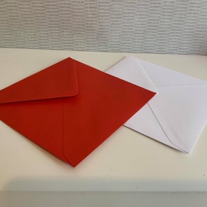 May include: Two envelopes, one red and one white, are lying flat on a white surface. The red envelope is on top of the white envelope.