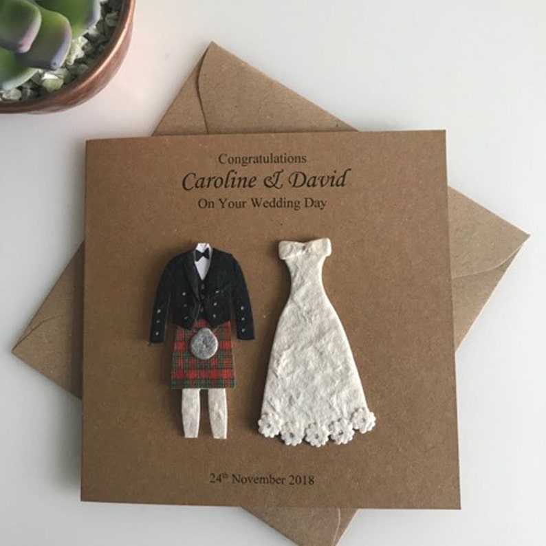K&ouml;nnte beinhalten: Eine braune Karte mit einer wei&szlig;en und schwarzen Illustration eines Brautpaares. Der Br&auml;utigam tr&auml;gt einen Kilt. Die Karte sagt "Herzlichen Gl&uuml;ckwunsch Caroline & David Zu Ihrem Hochzeitstag 24. November 2018".