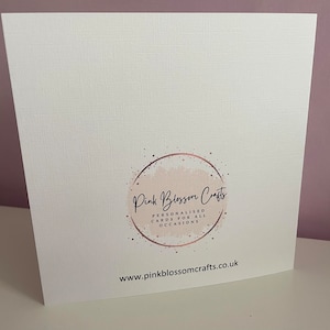 May include: A square white greeting card with a textured surface. The centre features a circular logo with a light pink watercolour wash, rose gold speckles, and the text Pink Blossom Crafts, Personalised Cards For All Occasions. The website www.pinkblossomcrafts.co.uk is printed in black at the bottom.