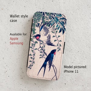 May include: A wallet style phone case with a floral design featuring two blue and white birds perched on branches. The case is available for Apple and Samsung phones. Model pictured: iPhone 11.