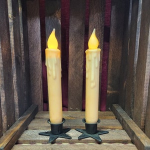 May include: Two lit, drippy, wax candles with black metal star-shaped bases, sitting in a wooden crate.