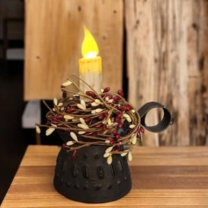May include: A black metal candle holder with a battery-operated candle. The candle is surrounded by a decorative wreath of red and white berries. The candle has a flickering yellow flame.