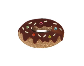 Puede incluir: Una dona cubierta de chocolate con chispas y joyas de colores. La dona está hecha de purpurina marrón y tiene un glaseado blanco.