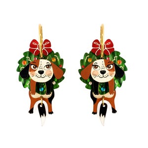 Puede incluir: Un par de pendientes colgantes con un diseño de perro beagle de dibujos animados. El perro está rodeado por una corona verde con un lazo rojo. Los pendientes tienen aros dorados y están sobre un fondo blanco.