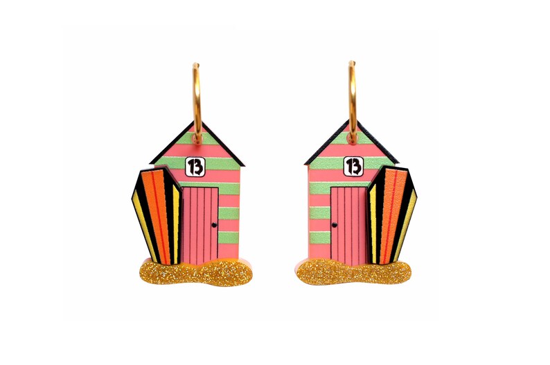 May include: A pair of pink and green beach hut earrings with gold hoops. Each earring features a surfboard and the number "13" on the front of the hut.