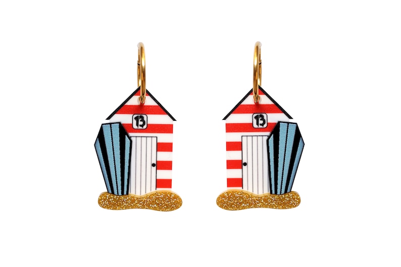 May include: A pair of red and white striped beach hut earrings with blue and white striped beach umbrellas. The earrings have gold hoops and glitter accents.