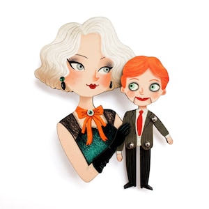 May include: Illustration of a woman with white hair and a ventriloquist dummy. The woman wears a black dress with an orange bow and black gloves. The dummy has red hair, a suit, and a red tie. The artwork has a vintage style.