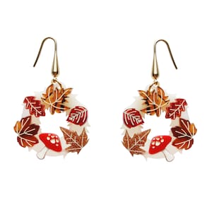 May include: A pair of gold earrings with a white base and a wreath of autumn leaves and red mushrooms.