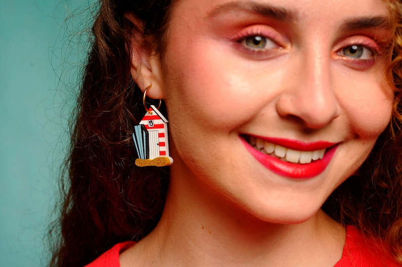 May include: A pair of gold hoop earrings with a red, white, and blue beach hut charm. The charm has a number "13" on the side.