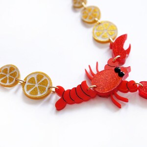 May include: A red lobster charm necklace with gold glitter lemon slices. The lobster is red with black eyes and has a gold chain.