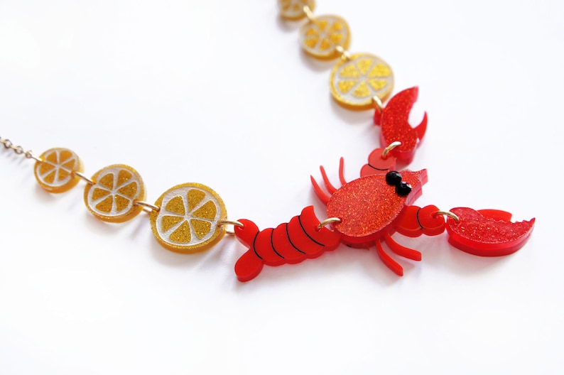 May include: A red lobster charm necklace with gold glitter lemon slices. The lobster is red with black eyes and has a gold chain.