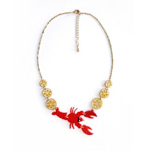 May include: A gold chain necklace with a red lobster charm and yellow lemon slice charms.