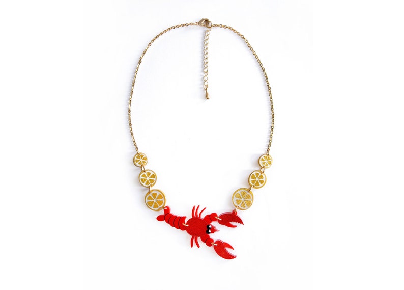 May include: A gold chain necklace with a red lobster charm and yellow lemon slice charms.