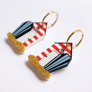 May include: A pair of gold hoop earrings with red and white striped beach hut charms. The huts have blue doors and windows and the number "13" is printed on the side.