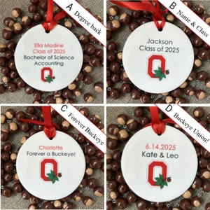 May include: Four white round ornaments with red ribbon and a buckeye nut garland. The ornaments feature the Ohio State University logo and personalized text. The text on the ornaments reads: "Ella Modine Class of 2025 Bachelor of Science Accounting", "Jackson Class of 2025", "Charlotte Forever a Buckeye!" and "6.14.2025 Kate & Leo".