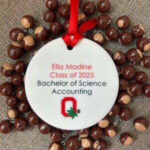 May include: White ceramic ornament with red ribbon, featuring the text "Ella Modine Class of 2025 Bachelor of Science Accounting" and the Ohio State University logo.