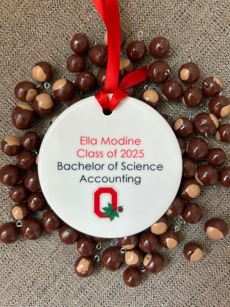 May include: White ceramic ornament with red ribbon, featuring the text "Ella Modine Class of 2025 Bachelor of Science Accounting" and the Ohio State University logo.