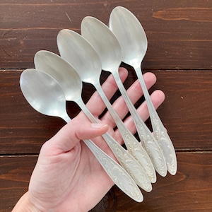 Pode incluir: Um conjunto de seis colheres de prata com detalhes florais ornamentados nos cabos. As colheres estão dispostas em forma de leque, mostrando suas superfícies polidas. Perfeitas para servir.