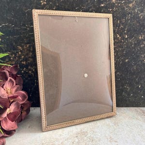 May include: A rectangular picture frame with a metallic gold finish and a textured zigzag pattern along the border. The frame features a clear glass front panel and a simple, clean design, providing a neutral display for photographs or artwork.
