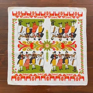 Pode incluir: Têxtil quadrado branco com um design de arte popular. O design apresenta músicos tocando violino, motivos de cavalos e padrões florais em vermelho, verde e amarelo. O têxtil tem uma borda de elementos decorativos verdes e vermelhos.