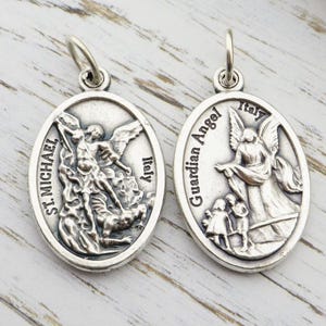 May include: Two silver oval pendants. One pendant depicts St. Michael slaying a demon, with "St. Michael" and "Italy" inscribed. The other shows a guardian angel with children, inscribed with "Guardian Angel" and "Italy".