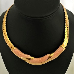May include: A gold chain necklace with a pink enamel design. The necklace is on a black mannequin bust.