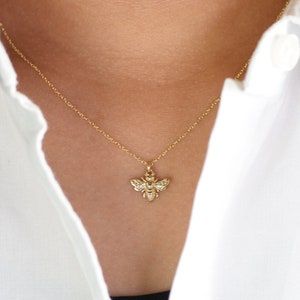 May include: A gold chain necklace with a small bee pendant. The bee is detailed with textured wings and a body.