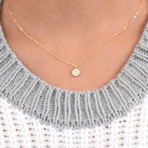 K&ouml;nnte beinhalten: Eine zarte goldene Kettenkette mit einem kleinen, runden Anh&auml;nger mit einem detaillierten Blumenmuster.