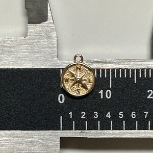 K&ouml;nnte beinhalten: Ein goldfarbener Kompass-Anh&auml;nger mit detailliertem Design. Der Kompass hat einen Durchmesser von etwa 1 cm und eine &Ouml;se oben zum Anbringen an einer Halskette oder einem Armband.