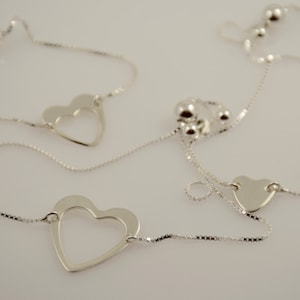 May include: A silver necklace with two open heart charms and a silver chain. The necklace has a sliding clasp for adjusting the length.
