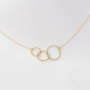 May include: A gold necklace with three interlocking circles. The circles are made of twisted wire.