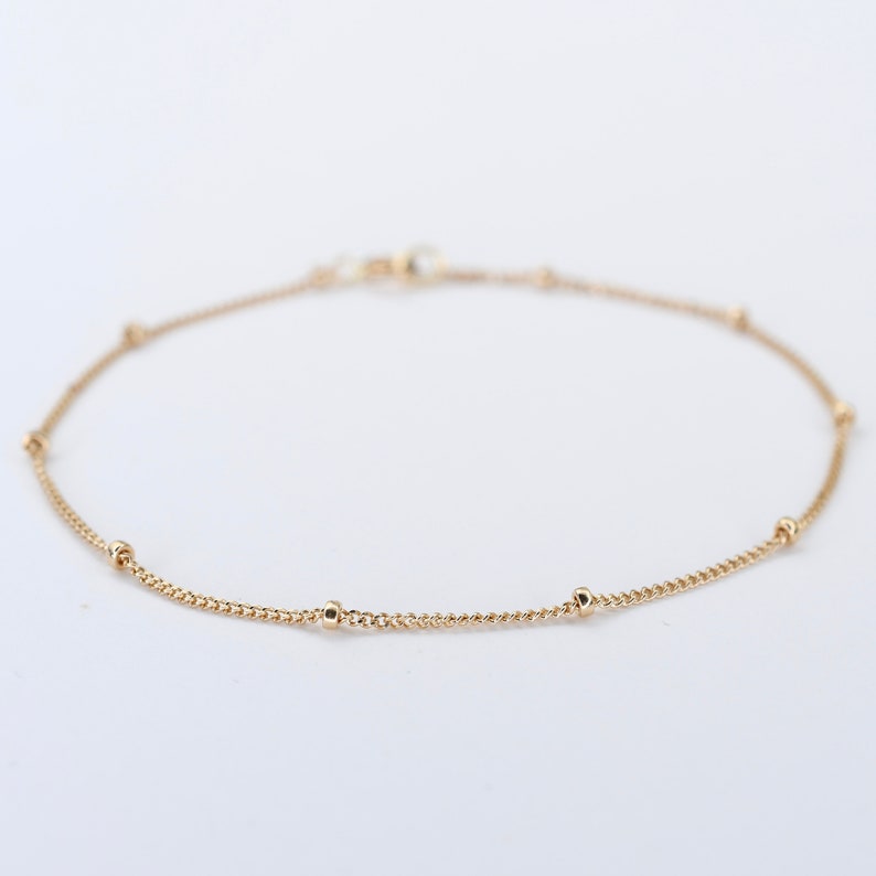 May include: A delicate gold chain bracelet with small round beads spaced evenly along the chain.