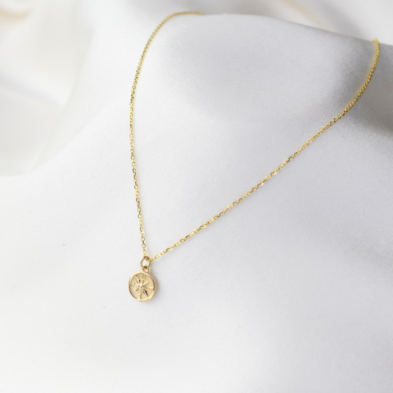 K&ouml;nnte beinhalten: Eine goldene Kettenkette mit einem kleinen, runden Anh&auml;nger mit einem Sonnendesign.