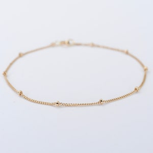 May include: A delicate gold chain anklet with small round beads.