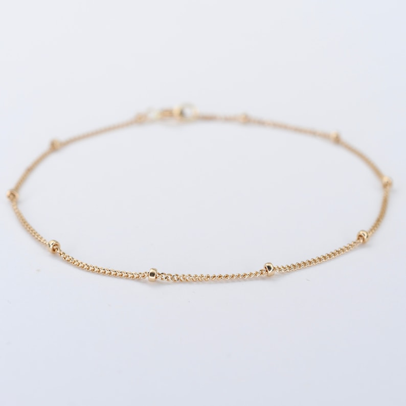 May include: A delicate gold chain anklet with small round beads.