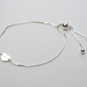 May include: A silver heart charm bracelet with a sliding bead closure. The heart charm has the letter "M" engraved on it.