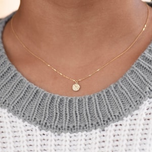 K&ouml;nnte beinhalten: Eine zarte goldene Kettenkette mit einem kleinen, runden Anh&auml;nger mit einem detaillierten Sternmuster.