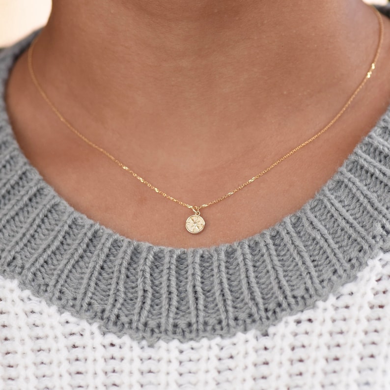K&ouml;nnte beinhalten: Eine zarte goldene Kettenkette mit einem kleinen, runden Anh&auml;nger mit einem detaillierten Sternmuster.