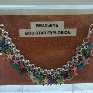 May include: A silver charm bracelet with a clasp closure. The bracelet is adorned with colorful star-shaped charms. The bracelet is displayed on a brown background with the text "BEADeEYE MOD STAR EXPLOSION".