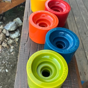 May include: A collection of five colorful skateboard wheels in shades of yellow, red, orange, blue, and green. Each wheel has a central hole and the text "GRIPTONIC 70 MM" and "LOTUS" printed on the side.