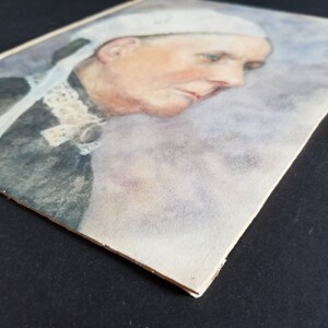 May include: A watercolour painting of a woman wearing a white cap and a dark dress. The woman is looking down and her face is partially obscured by the cap. The background is a soft, muted blue.