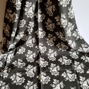 Op de afbeelding: Zwarte stof met een wit bloemenpatroon. De bloemen zijn gestileerd en lijken op bellen.