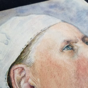 May include: Close-up of a watercolour painting of a person's face. The person is wearing a white cap and has blue eyes. The painting is done in a realistic style.