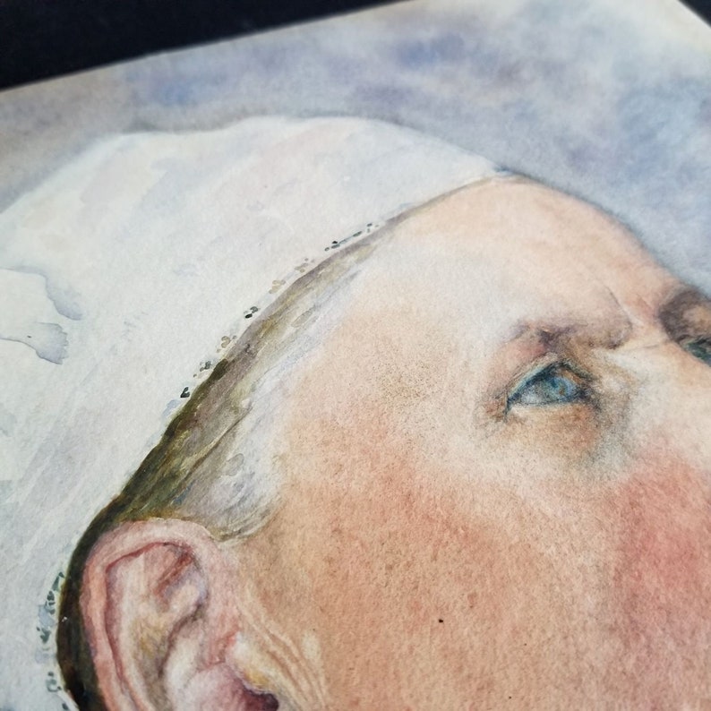 May include: Close-up of a watercolour painting of a person's face. The person is wearing a white cap and has blue eyes. The painting is done in a realistic style.