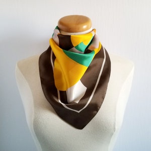 May include: A square silk scarf with a geometric design. The scarf features a brown border with a white outline, and a central pattern of yellow, green, and white shapes. The scarf is draped on a mannequin.