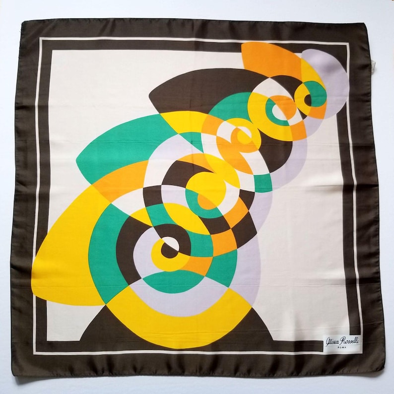 May include: Square silk scarf with a geometric design in shades of brown, yellow, green, orange, and lavender. The scarf has a white center with a dark brown border and a thin white inner border. The designer's signature is in the bottom right corner.