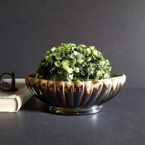 May include: A brown and cream ceramic planter with a silver base, featuring a fluted design. The planter is filled with a green artificial plant.